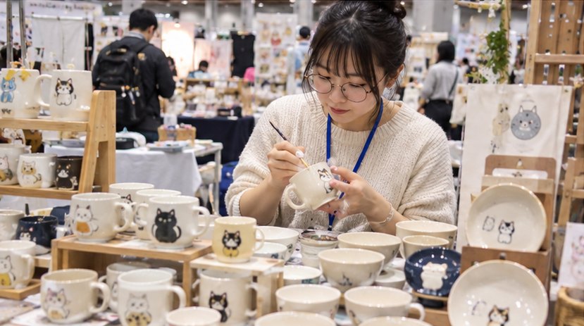 猫の絵柄のマグカップに絵付けをする出展者